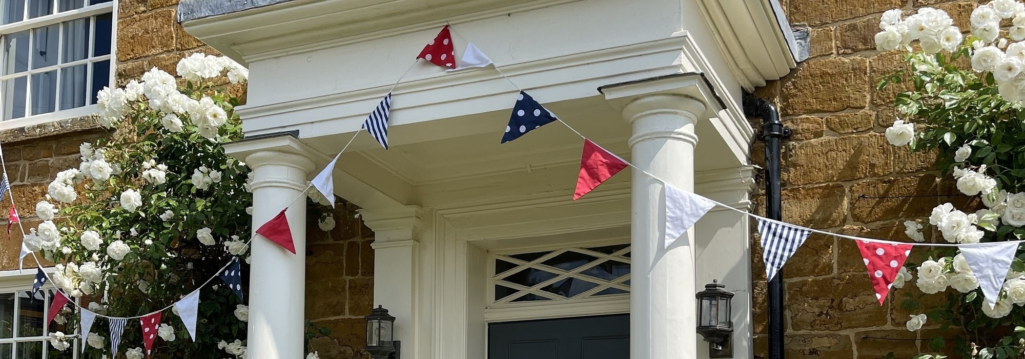 Trooping of the colour bunting with Iceberg climbing rose. David Austin Roses
